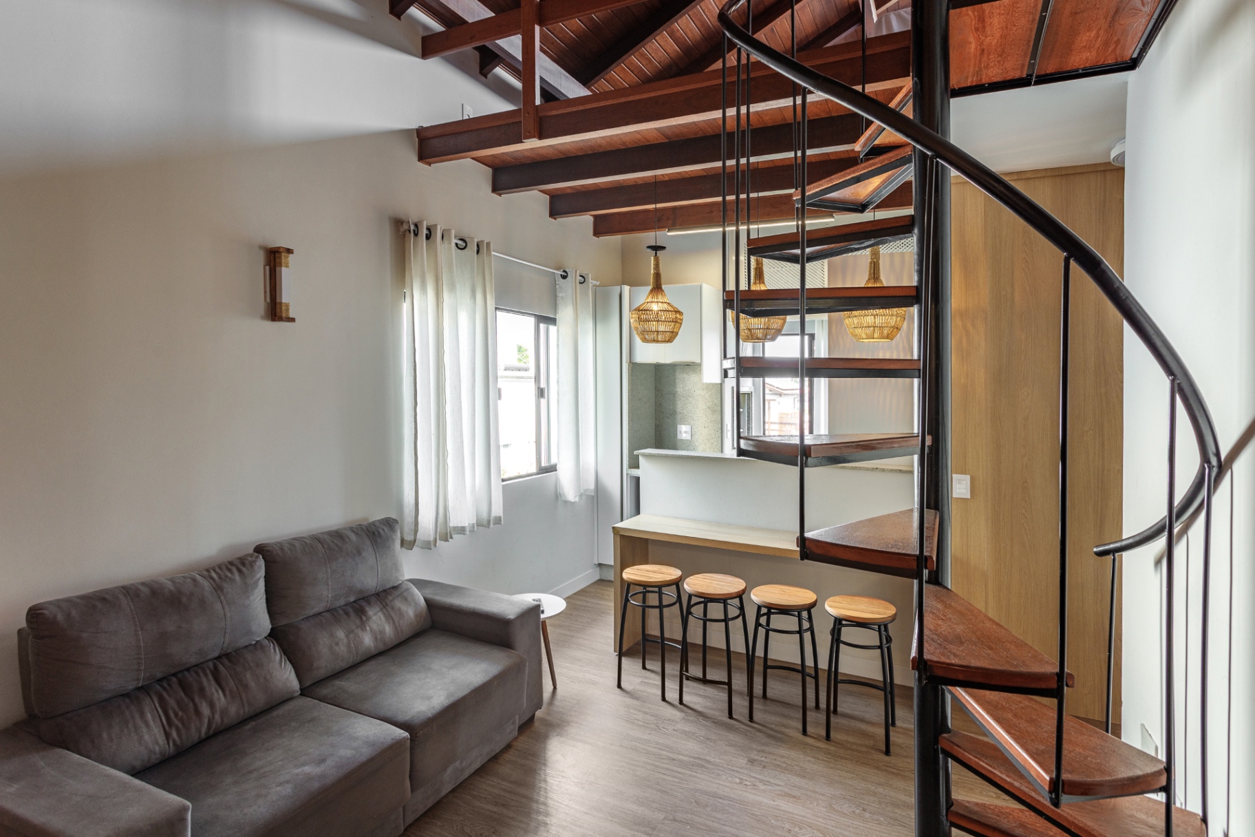 Sala integrada do Loft 203 com escada caracol e cozinha ao fundo