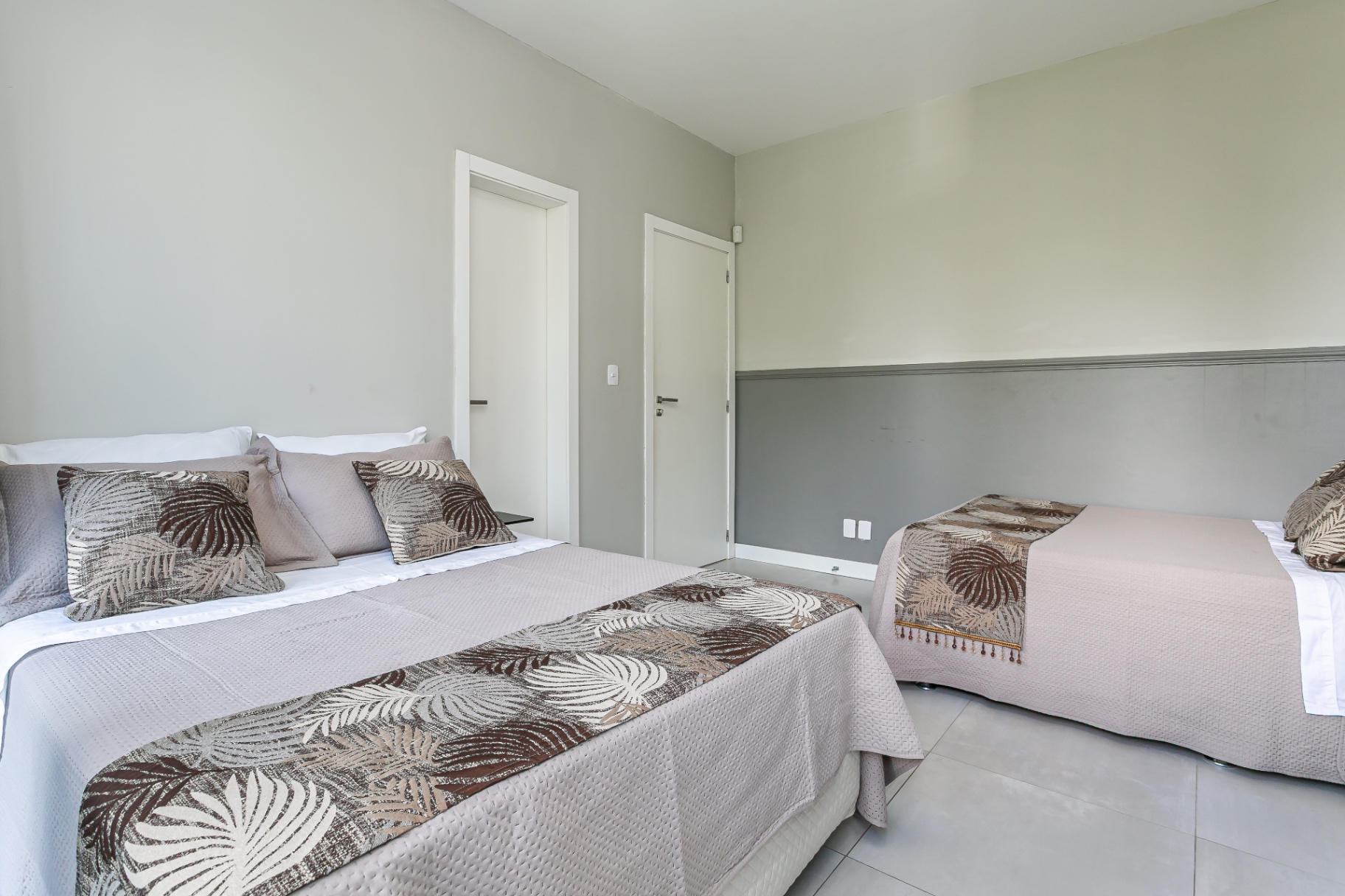 Quarto da Casa Noah com cama de casal e uma de solteiro em tons neutros