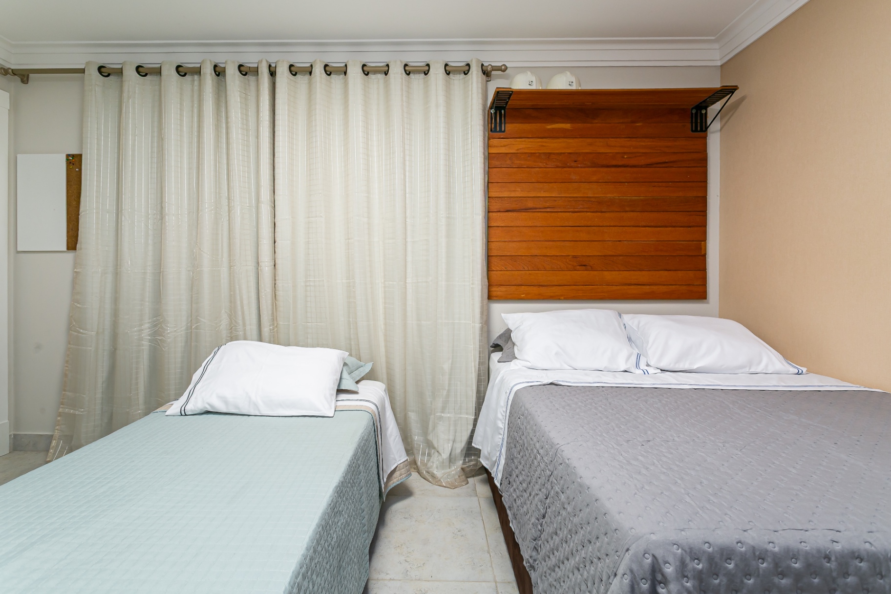Quarto da Casa Nevi com cabeceira de madeira e cortinas leves